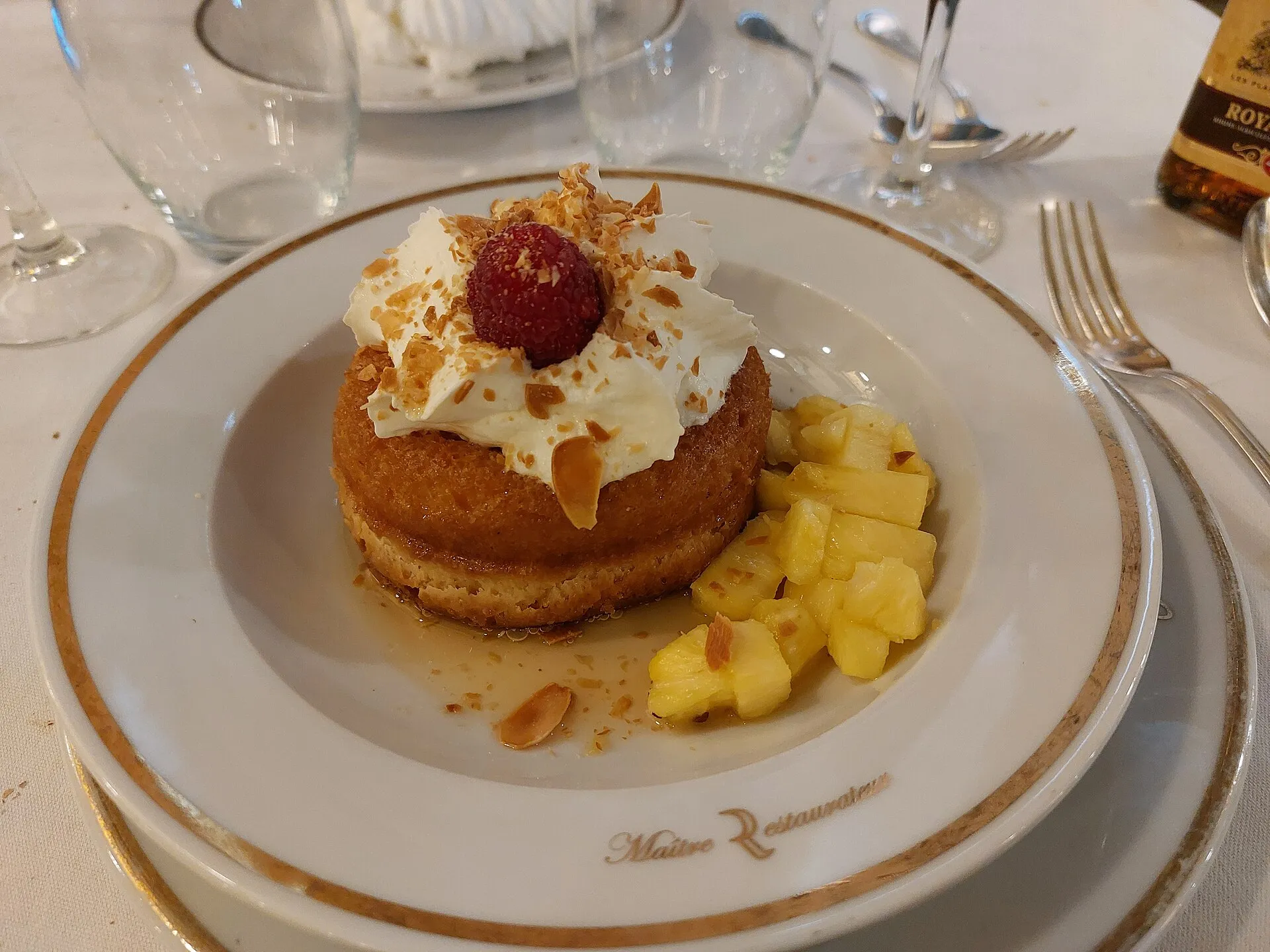 Baba au rhum de brasserie garni de chantilly, d'ananas rôti et de framboise, servi avec sa fiole de rhum