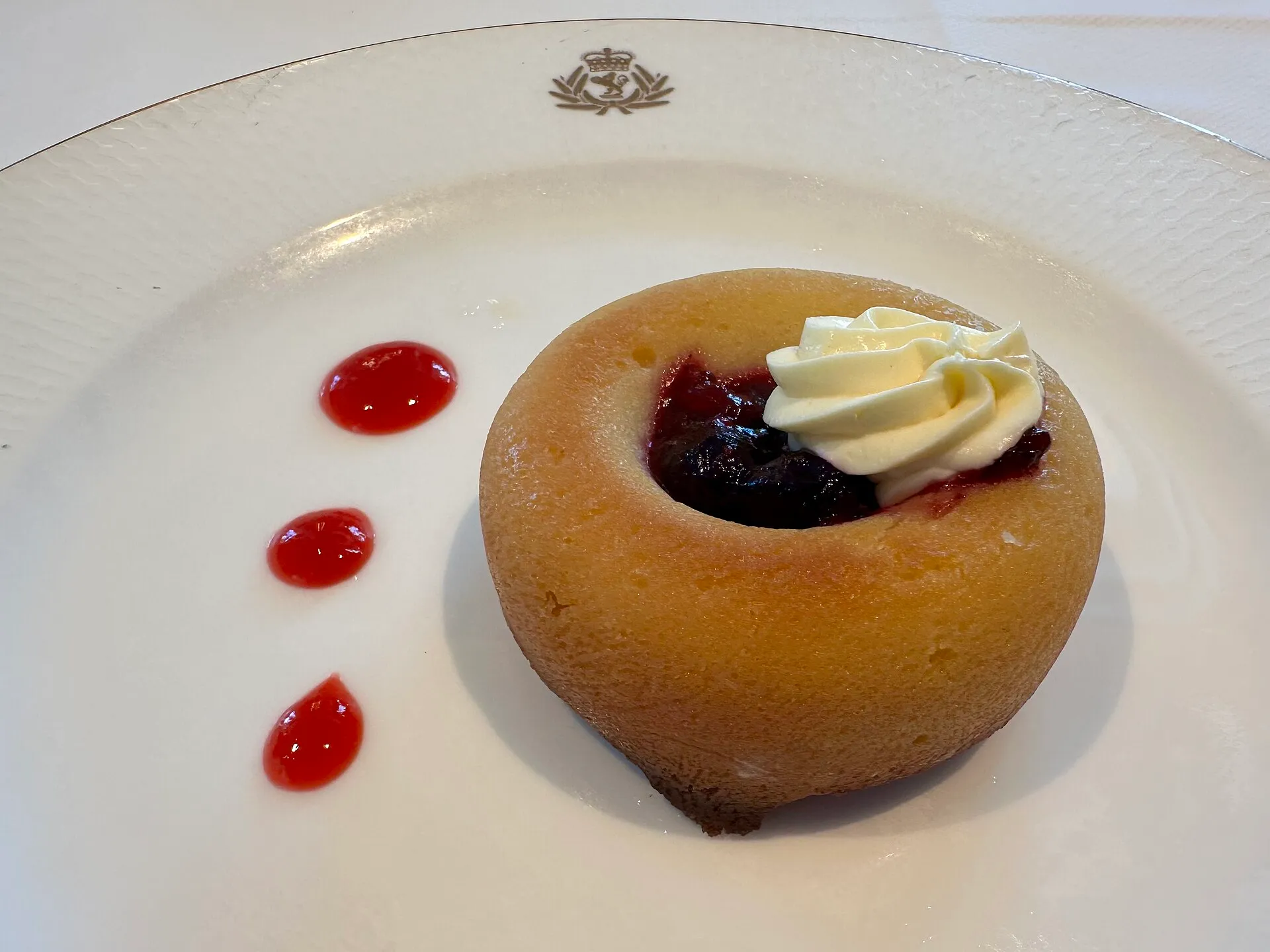 Baba bouchon garni de crème et d'une compotée de fruits rouges, servi sur une assiette à monogramme