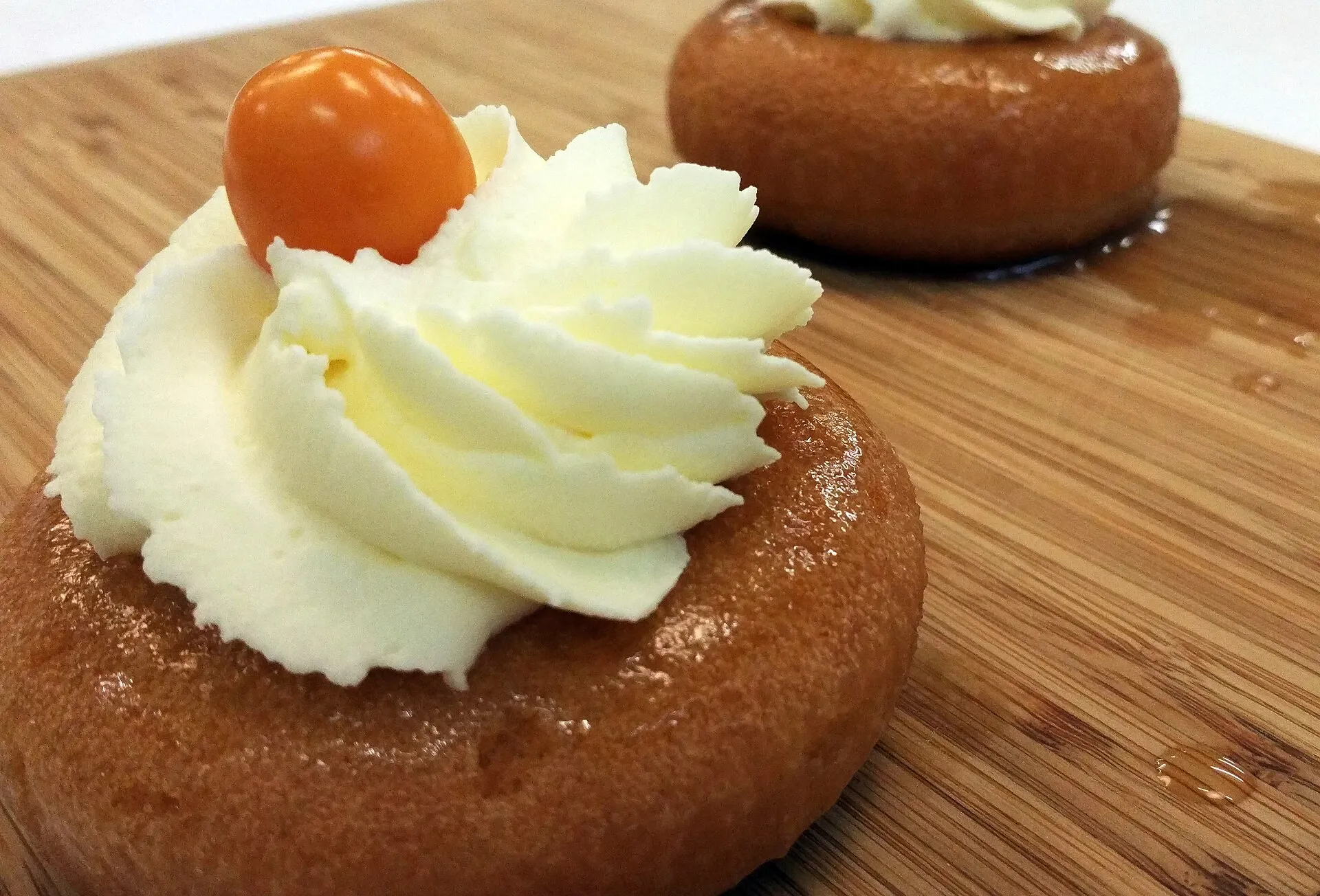 Deux mini-babas brillants de sirop, coiffés de chantilly et d'un physalis, sur une planche en bois