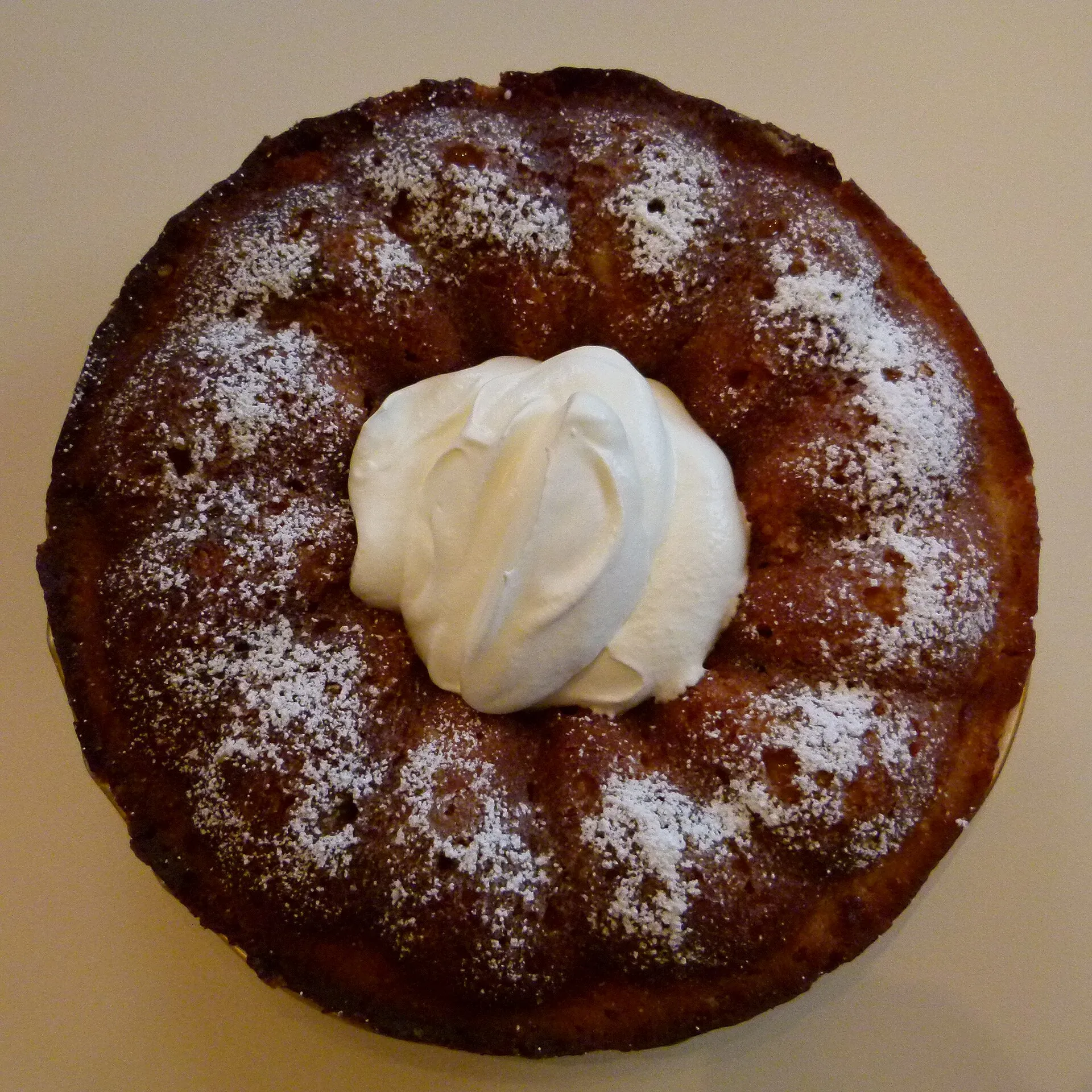Savarin entier saupoudré de sucre glace, le centre de la couronne garni de crème fouettée